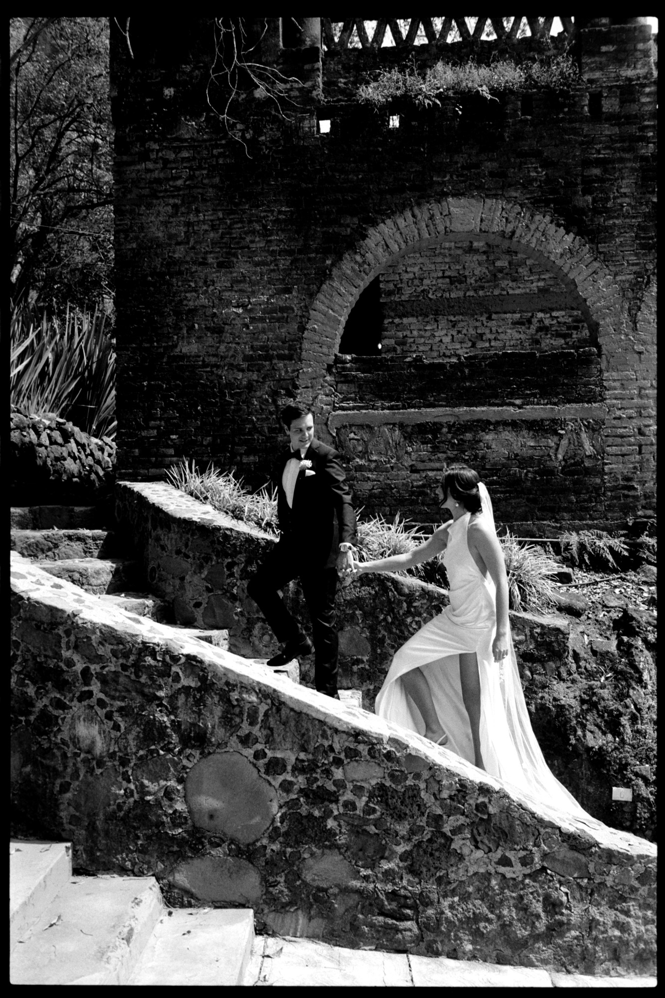 Couple walking up old stone steps under an arch, black and white film